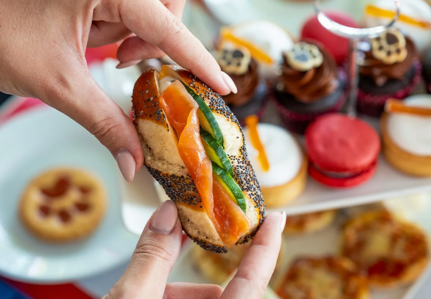 A hand selecting a sandwich from a themed afternoon tea spread